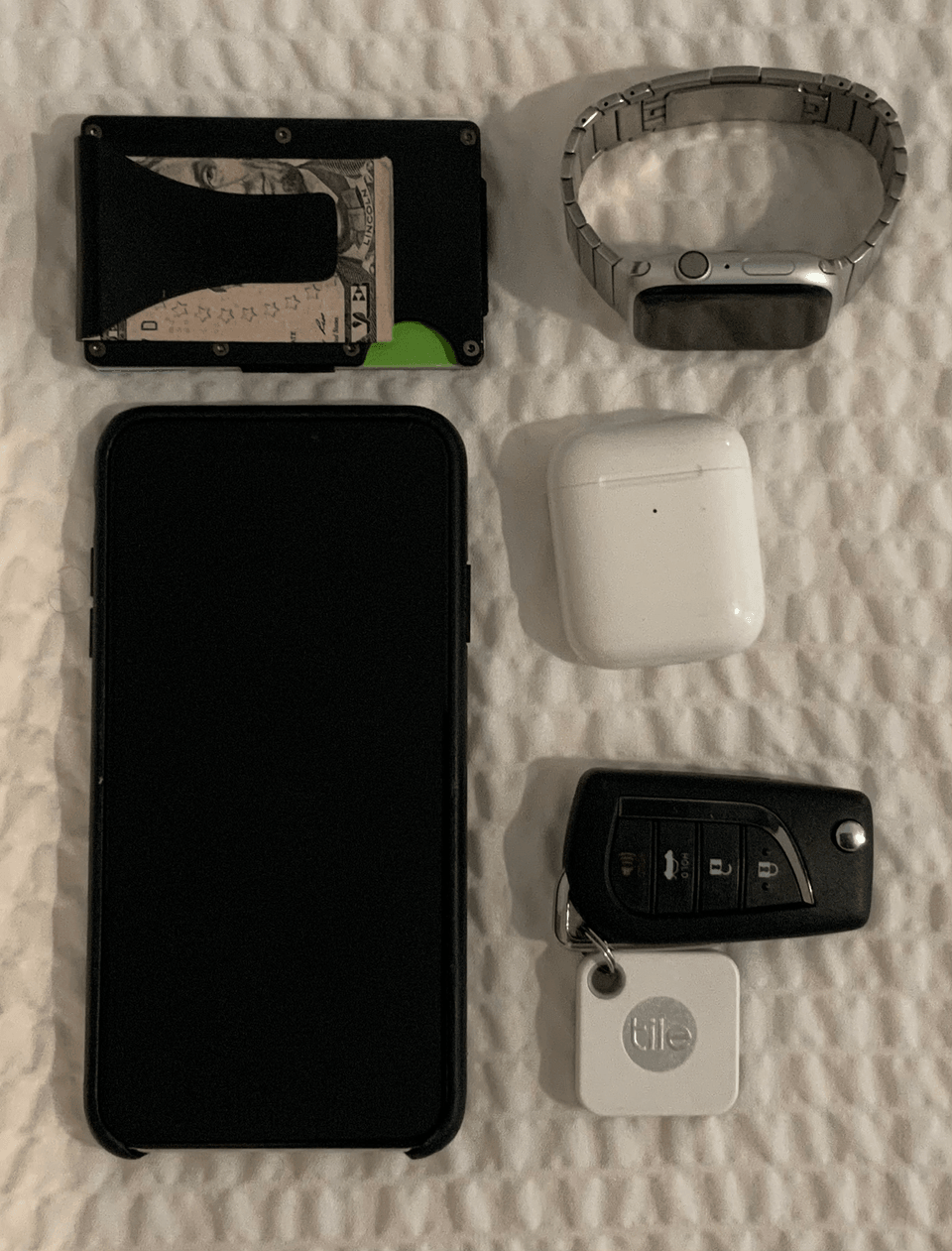 Layflat knolling of phone, keys, wallet, AirPods and tile. 